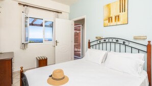 Un dormitorio con cama, ventana con vistas, puerta, una obra de arte colgada en la pared y un sombrero sobre la cama.
