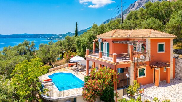 Una casa de dos pisos con piscina, rodeada de vegetación y con vista a un cuerpo de agua.