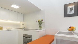 Eine kompakte Küche mit weißen Schränken, einem eingebauten Backofen, einer Spüle und einer kleinen Essecke mit einer Bank.