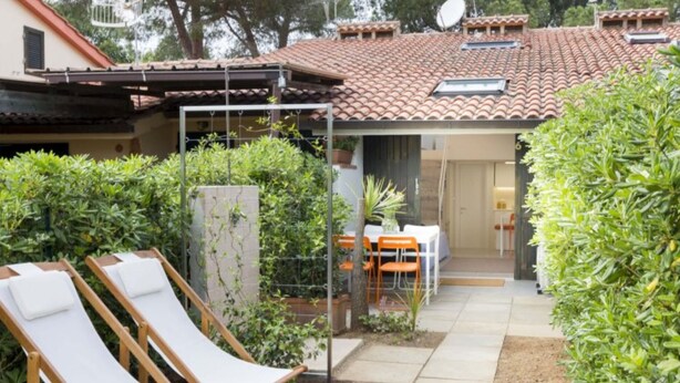 Eine Terrasse mit zwei Liegestühlen, einem Tisch und Stühlen, umgeben von Grünpflanzen.