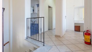 A hallway with a staircase, a fire extinguisher, and a kitchen area with cabinets.