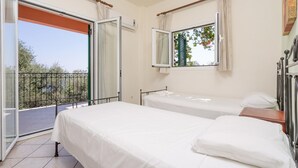 A bedroom with two beds, a balcony, and a window with a view of greenery.