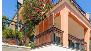 A two-story building with a stone wall entrance, a balcony with metal railings, and a sign indicating "Villa Vasillis."