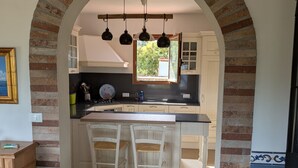 A kitchen with an archway, wooden chairs, a stove, and a window with a view. - Independent villa with splendid sea view terrace (Capoliveri)