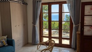 A room with a view of the sea, a blue sofa, a wicker chair, a wooden cabinet, and a tiled floor. - Independent villa with splendid sea view terrace (Capoliveri)
