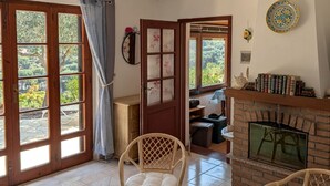 A room with a fireplace, wicker chairs, a table with a remote, and a view through large windows. - Independent villa with splendid sea view terrace (Capoliveri)