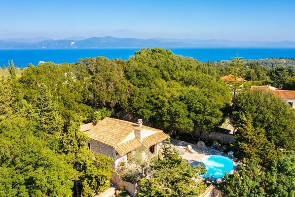 Eine Villa mit Natursteinfassade, umgeben von üppiger Vegetation und einem klaren, blauen Meer im Hintergrund.