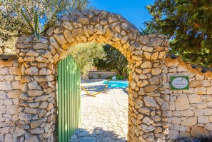 A stone archway leading to a pool area with a sign indicating 'Villa Nionios'.