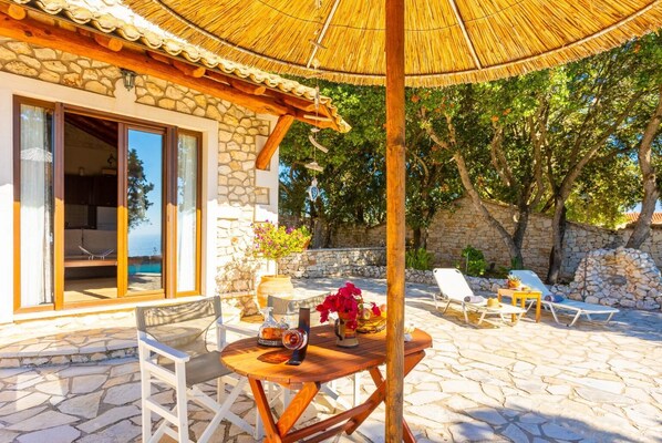 Ein Steinhaus mit einer Terrasse, inklusive Tisch, Stühlen und Liegestühlen.