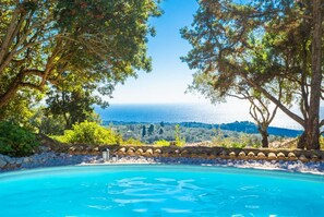 A pool with a clear view of the sea and a stone wall with lanterns.