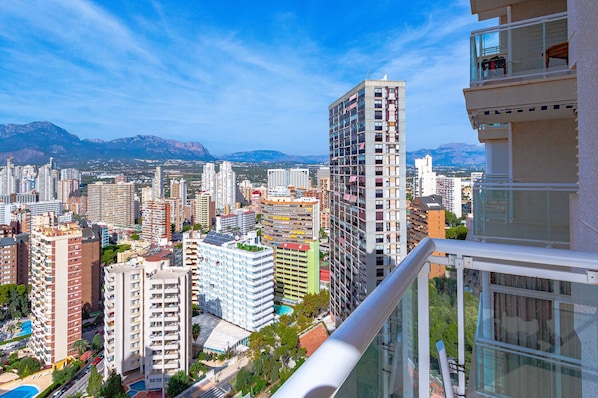 A high-rise building with multiple balconies and a view of a cityscape with mountains in the background.