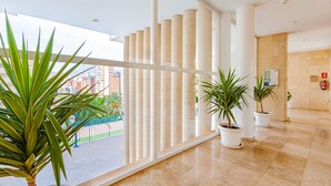 Un hall d’hôtel moderne, doté de grandes fenêtres, de plantes en pot et offrant une vue sur le paysage urbain.