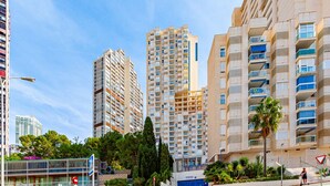 Un immeuble résidentiel de grande hauteur doté de nombreux balcons, d’une promenade piétonne et entouré de verdure.