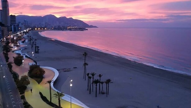 Une vue d’une ville côtière au crépuscule, avec une promenade incurvée menant à une plage.