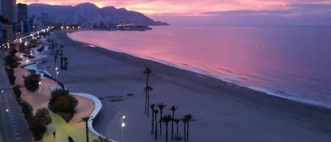 Un paisaje urbano costero al atardecer, con una rambla curva que conduce a una playa.