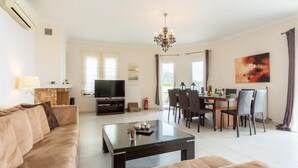 A modern living room with a sofa, a coffee table, a TV, and a dining area with chairs and a table.