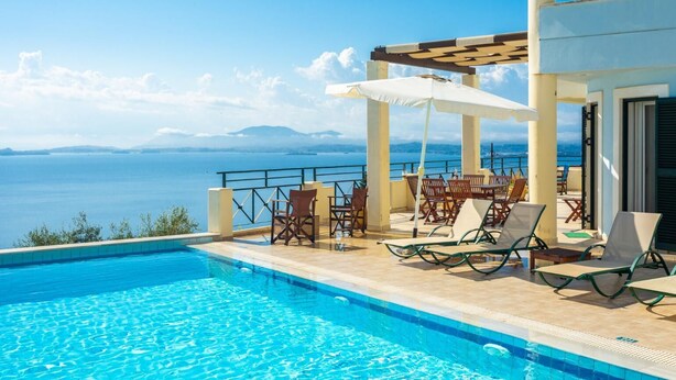 A swimming pool with a view of the sea, outdoor seating, and a pergola.
