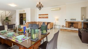 A modern living room with a fireplace, a dining area with a glass table, and a staircase leading to another level.