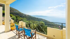 A balcony with a view of a coastal landscape, including a sea and hills.