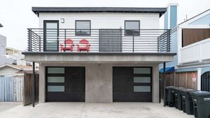 A modern building with a flat roof, two garage doors, and a balcony with red chairs. - Newport Beach Modern Home steps to the Beach (Newport Beach)