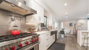A modern kitchen with a stainless steel stove, white cabinetry, and a brick backsplash. - Newport Beach Modern Home steps to the Beach (Newport Beach)