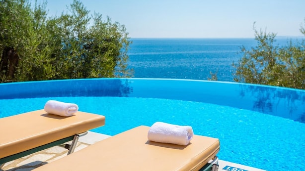 Una piscina sense fi amb dos relaxants i tovalloles, envoltada de vegetació i amb vista al mar.