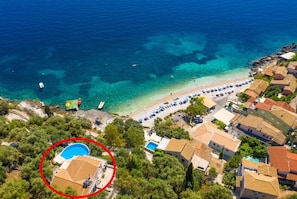 Vista aérea de una zona costera con playa, aguas azules cristalinas y un barrio residencial.