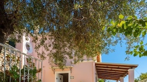 Una escala de pedra que condueix a un edifici amb façana rosa, una zona d'estar a l'aire lliure coberta i una pèrgola.