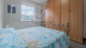 Un dormitorio con cama, armario, ventana y silla.