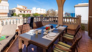 Een balkon met een eettafel voor vier personen, rieten stoelen en uitzicht op zee.