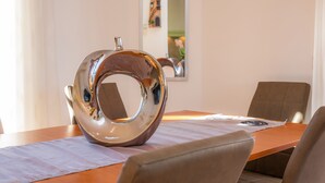 Een eettafel met een glimmend metalen voorwerp, een ingelijst foto aan de muur, en een stoel.