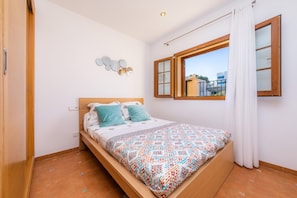 Ein Schlafzimmer mit einem hölzernen Bett, weißen Wänden, einem Fenster mit Vorhängen und Blick auf Gebäude.