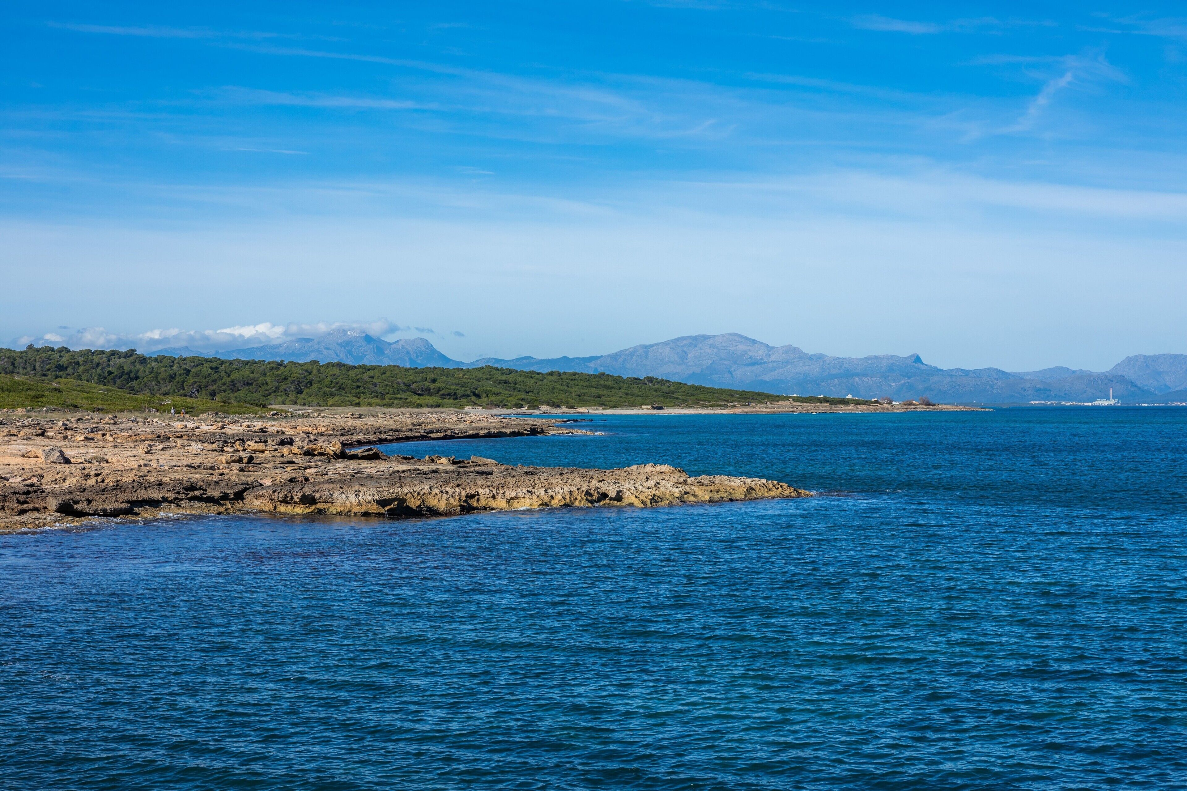 Un paysage côtier caractérisé par des rivages rocheux, une mer calme et des montagnes lointaines.