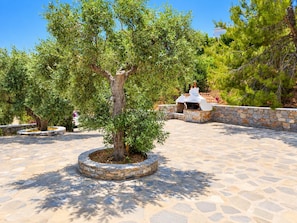 A stone-paved outdoor area with a central tree, stone walls, and a white outdoor kitchen.