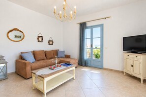Un salon comprenant un canapé, une table basse, un téléviseur et une porte donnant sur un balcon.