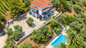 Une maison à deux étages, avec un toit en tuiles, entourée d’un mur de pierre et agrémentée d’une piscine.