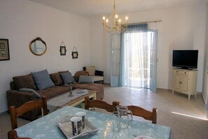 A living room with a sofa, a dining table with chairs, a television, and a chandelier. - Villa Ourania - Three Bedroom Villa, Sleeps 6 (Sporades)