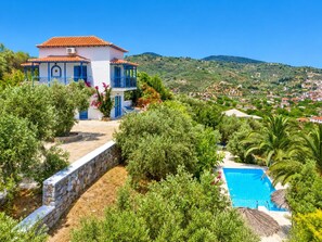 A two-story building with a pool, surrounded by lush greenery and hills in the background.