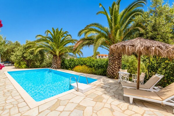 A swimming pool with lounge chairs and a thatched umbrella.
