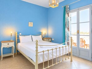 A bedroom with a bed, bedside tables, a nightstand, a wall-mounted lamp, and a view through a door.