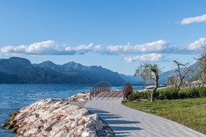 Ein gepflasterter Weg führt zu einer Brücke über ein Gewässer, im Hintergrund Berge.