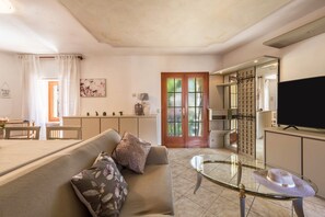 A living room with a sofa, a glass coffee table, a television, and a dining area with a table and chairs.