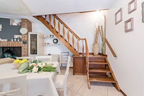 Eine Treppe mit Holzhandläufen, ein Essbereich mit Tisch und Stühlen sowie eine Küche mit Schränken und einer Uhr.