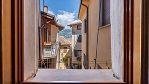 Ein schmaler Straßenblick durch ein Fenster, mit Gebäuden an beiden Seiten und blauem Himmel.