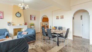 Un vaste salon agrémenté d’une cheminée, un coin repas avec une table dressée pour quatre personnes, et une cuisine visible à travers une arche.