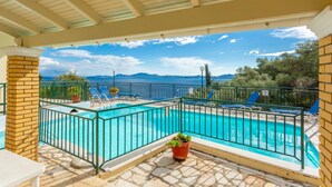 Une piscine à l’eau d’un bleu cristallin, entourée d’une clôture métallique, et offrant une vue panoramique sur la mer et les montagnes.