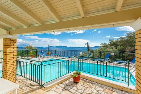 Ein Poolbereich mit klarem, blauem Wasser, umgeben von einem Metallzaun und mit Blick auf eine malerische Landschaft aus Meer und Bergen.