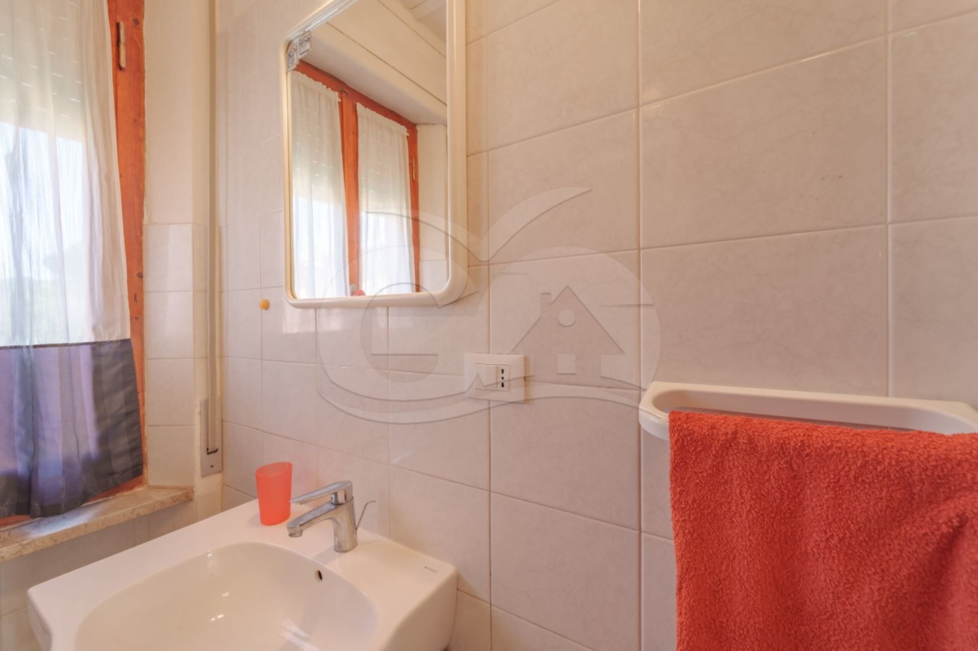 Une salle de bain avec un lavabo blanc, un miroir et une serviette rouge.