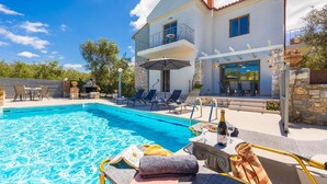 A poolside area with lounge chairs, a table with a bottle and glasses, and a book. - Villa Tzina - Three Bedroom Villa, Sleeps 6 (Tavronitis)