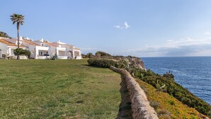 Una propiedad costera con edificios blancos, un muro de piedra y vista al mar.